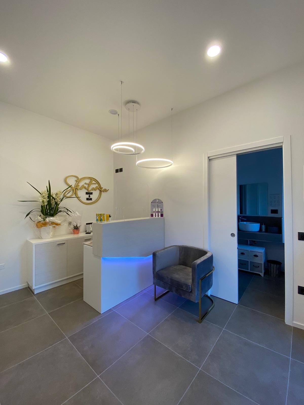 L'ingresso del centro: il bancone bianco illuminato di blu, una poltroncina di velluto grigio, il logo Sintonia dorato sulla parete e un'orchidea bianca