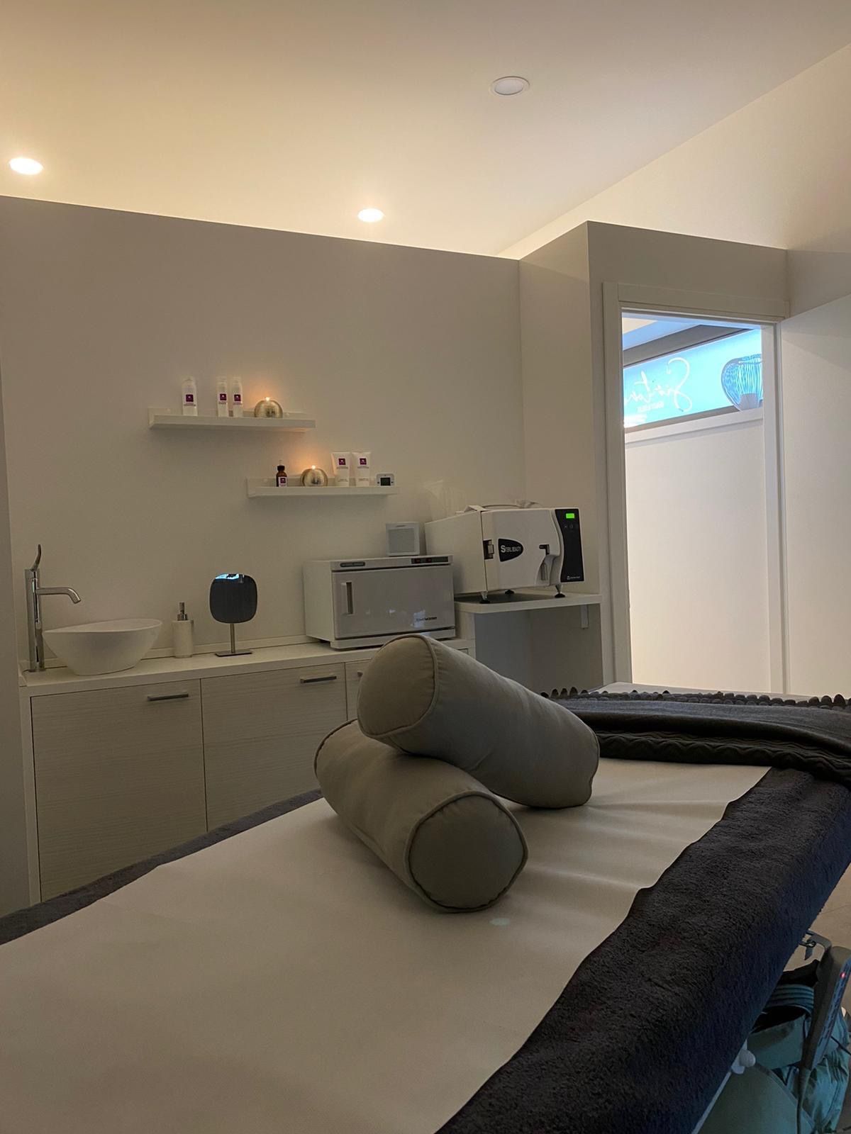 La cabina a luce soffusa: il lettino con due cuscini a rullo e la coperta scura, le candele accese sulle mensole dei prodotti